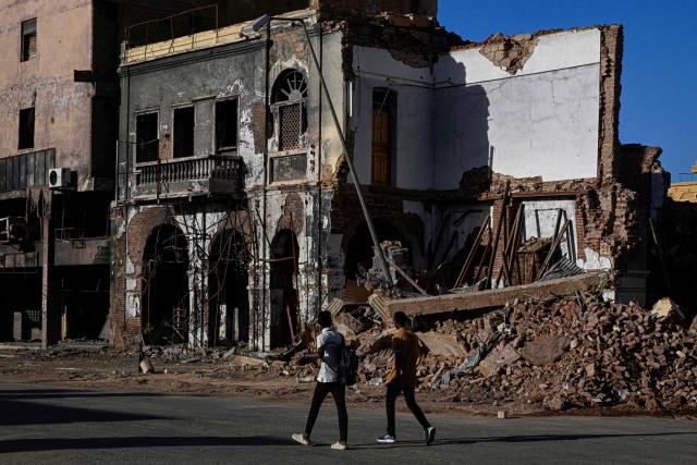 Sudanese men walk past destroyed building in the capital Khartoum on April 16, 2026. Of the nearly four million people -- around half Khartoum's pre-war population -- who fled during the conflict, more than 1.8 million have returned over the past year. Yet fewer than 80,000 people have come back to central Khartoum, according to the United Nations. (Photo by Khaled DESOUKI / AFP)