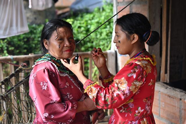 Etelbina Queragama Guatiqui (L), 63, an Embera Chami Indigenous woman and homemaker, is made up by her daughter Maruilla before an interview with AFP in Vereda Tuma Drua, in the unified Embera Chami Rio San Juan reservation, Pueblo Rico, Risaralda, Colombia, on April 9, 2026. In the coffee-growing mountains of the Risaralda department in western Colombia, ancestral territory of the Embera Chami and Katio peoples, genital mutilation affects hundreds of girls. (Photo by Diana SANCHEZ / AFP)