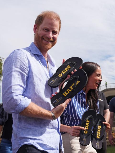 Britain's Prince Harry, Duke of Sussex, and his wife Meghan, the Duchess of Sussex, react after they received flip-flops with the inscriptions "G'day Hazza" and "G'day Megs" from veteran Joel Vanderzwan and his family after taking part in a sailing event with members of Invictus Australia in Sydney Harbour on April 17, 2026. (Photo by Jonathan Brady / POOL / AFP)