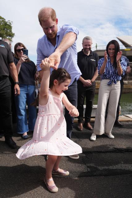 Britain's Prince Harry, Duke of Sussex, twirls Charlotte, the daughter of veteran Joel Vanderzwan, as his wife Meghan, the Duchess of Sussex, claps before taking part in a sailing event with members of Invictus Australia in Sydney Harbour on April 17, 2026. (Photo by Jonathan Brady / POOL / AFP)