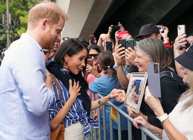 A woman presents Britain's Prince Harry, Duke of Sussex, with a framed photograph of him with her mother Daphne Dunn, as he and his wife Meghan (C), the Duchess of Sussex, arrive at the Man O'War Steps next to the Sydney Opera House before taking part in a sailing event with members of Invictus Australia in Sydney Harbour on April 17, 2026. (Photo by Jonathan Brady / POOL / AFP)