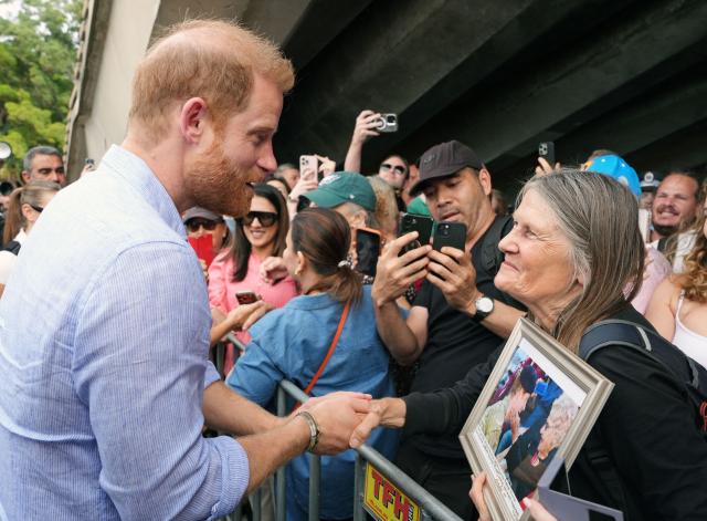 A woman presents Britain's Prince Harry, Duke of Sussex, with a framed photograph of him with her mother Daphne Dunn, as he arrives at the Man O'War Steps next to the Sydney Opera House before taking part in a sailing event with members of Invictus Australia in Sydney Harbour on April 17, 2026. (Photo by Jonathan Brady / POOL / AFP)