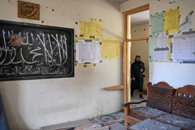 This photograph taken on April 13, 2026 shows a Taliban security personnel walking past a damaged classroom in a school that was struck by a Pakistani mortar shell during clashes between Taliban security personnel and Pakistani forces near the Durand Line in the Barikot village of Naray district, Kunar province. There are no children in the Afghan border village of Barikot, where the school has been smashed by shells and the playground sits deserted after weeks of war with Pakistan. More than 94,000 Afghans have been displaced by the war, OCHA figures show, more than a quarter of them in Kunar province. (Photo by Wakil KOHSAR / AFP)