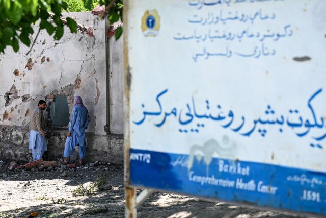 This photograph taken on April 13, 2026 shows Afghan medical personnel standing next to the damaged wall of a hospital hit by a Pakistani mortar shell during a conflict between Taliban security personnel and Pakistani forces near the Durand Line border between Pakistan and Afghanistan in the Barikot village of Naray district, Kunar province. There are no children in the Afghan border village of Barikot, where the school has been smashed by shells and the playground sits deserted after weeks of war with Pakistan. More than 94,000 Afghans have been displaced by the war, OCHA figures show, more than a quarter of them in Kunar province. (Photo by Wakil KOHSAR / AFP)