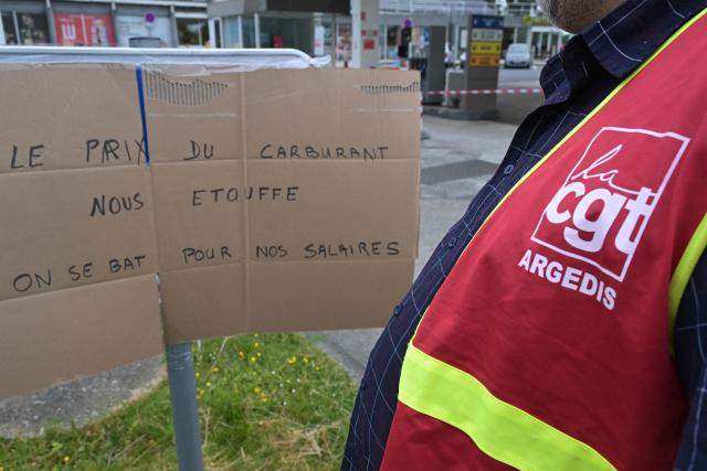 A worker on strike stands by a placard reading "Fuel prices are choking us: We are fighting for our salaries" pictured at a gas station blocked by Argedis employees to demand fuel assistance in Saint-Aubin-de-Terregatte, western France on April 17, 2026. The CGT union at Argedis, a TotalEnergies subsidiary that operates around 200 service stations, notably on motorways, has called on employees to strike on April 17, 2026 to demand financial assistance with fuel costs, amid soaring prices, the union said on April 16. (Photo by Damien MEYER / AFP)