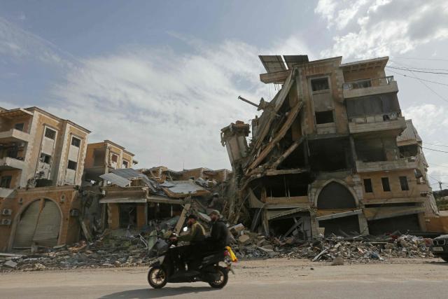 Displaced residents ride past a destroyed building as they return back to the southern Lebanese city of Nabatieh on April 17, 2026. A 10-day ceasefire deal struck between Lebanon and Israel took effect on April 17, sending displaced residents streaming south towards their homes, even as the Lebanese army warned of "a number of violations" in the area. (Photo by MAHMOUD ZAYYAT / AFP)