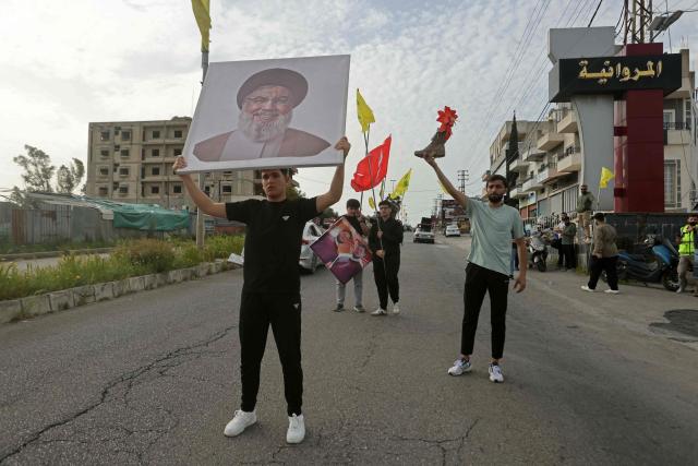A man holds a portrait of slain Hezbollah leader Hassan Nasrallah while celebrating the ceasefire, in the southern Lebanese town of Marwanieh on April 17, 2026. A 10-day ceasefire deal struck between Lebanon and Israel took effect on April 17, sending displaced residents streaming south towards their homes, even as the Lebanese army warned of "a number of violations" in the area. (Photo by MAHMOUD ZAYYAT / AFP)