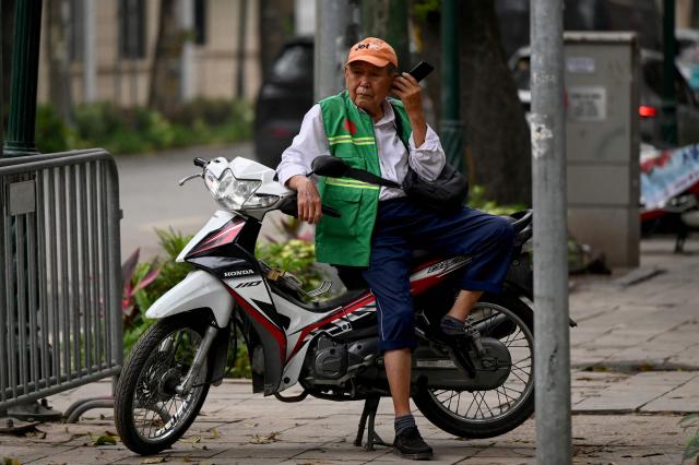 A motorbike taxi driver uses his phone while waiting for a passenger on a street in Hanoi on April 17, 2026. (Photo by Nhac NGUYEN / AFP)