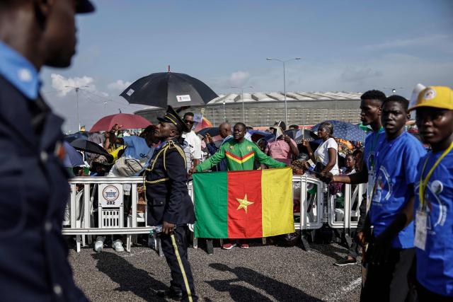 A man holds a Cameroonian flag as faithfuls gather ahead of the Holy Mass to be lead by Pope Leo XIV at the area in front of Japoma Stadium in Douala on the fifth day of an 11-day apostolic journey to Africa, on April 17, 2026. (Photo by Patrick MEINHARDT / AFP)