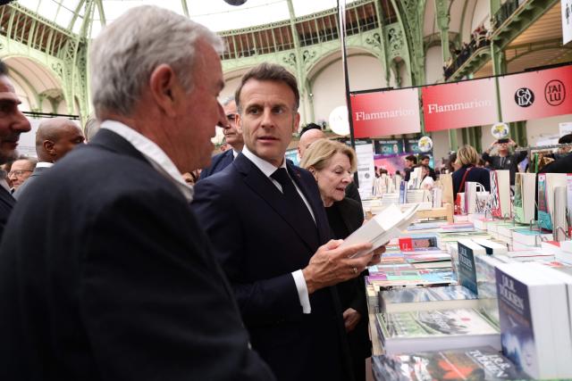 French President Emmanuel Macron (C) and Editions Gallimard publishing house president Antoine Gallimard (L) visit the Paris Book Fair at the Grand Palais in Paris on April 17, 2026. The fair, which runs until April 19, spotlights comic books as its central theme. (Photo by Teresa SUAREZ / POOL / AFP)