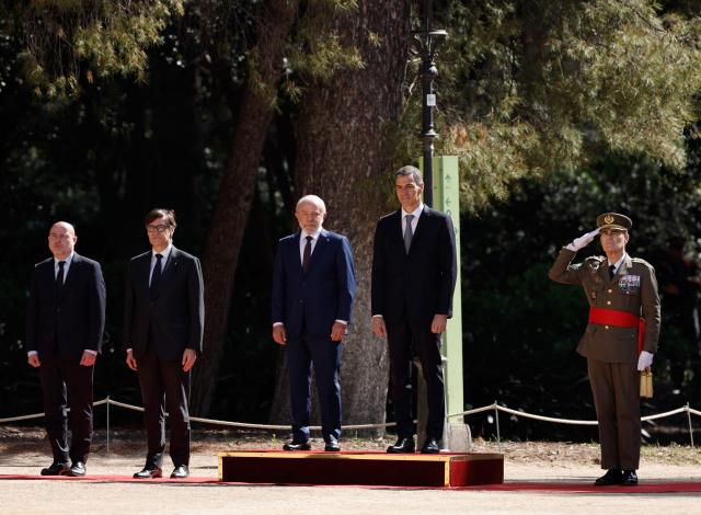 Spain's Prime Minister Pedro Sanchez (C,R) Brazilian President Luiz Inacio Lula da Silva (C,L) and Catalan regional president Salvador Illa (2R) attend a military ceremony held to welcome the Brazilian President at the Palacio de Pedralbes in Barcelona on April 17, 2026. Lula meets Spanish Prime Minister Pedro Sanchez and is to attend a forum of progressive leaders on April 18. Other attendees at the gathering in Barcelona include Mexican President and South African President. (Photo by Oscar DEL POZO / AFP)