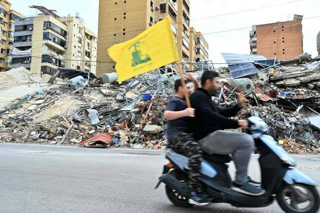 Residents carry a Hezbollah flag as they ride a motorcycle past destruction upon their return to their neighbourhood in Beirut's southern suburbs after a 10-day ceasefire with Israel came into effect on April 17, 2026. A 10-day ceasefire deal struck between Lebanon and Israel took effect on April 17, sending displaced residents streaming south towards their homes, even as the Lebanese army warned of "a number of violations" in the area. (Photo by FADEL itani / AFP)