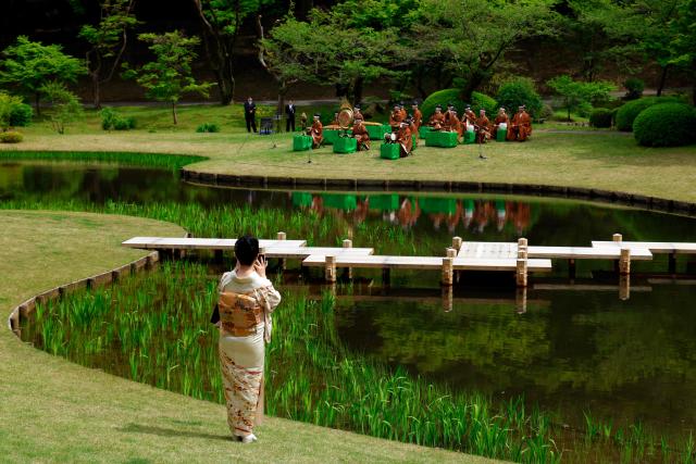 A guest takes pictures of musicians playing Gagaku, an ancient Japanese court music, during the spring imperial garden party at the Akasaka Palace's imperial garden in Tokyo on April 17, 2026. (Photo by Franck ROBICHON / POOL / AFP)