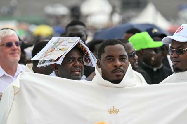 A Clergyman protects his head from the sun with a book on his head as they wait for Pope Leo XIV to arrive to lead the Holy Mass at the area in front of Japoma Stadium in Douala on the fifth day of an 11-day apostolic journey to Africa, on April 17, 2026. (Photo by Alberto PIZZOLI / AFP)