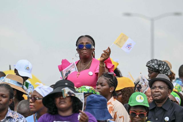 A faithful holds a Vatican flag as she attends the Holy Mass lead by Pope Leo XIV at the area in front of Japoma Stadium in Douala on the fifth day of an 11-day apostolic journey to Africa, on April 17, 2026. (Photo by Alberto PIZZOLI / AFP)