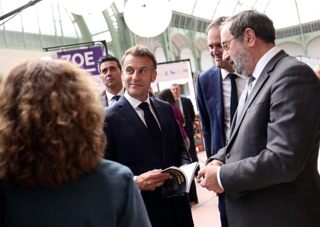 French President Emmanuel Macron (C) visits the Paris Book Fair at the Grand Palais in Paris on April 17, 2026. The fair, which runs until April 19, spotlights comic books as its central theme. (Photo by Teresa SUAREZ / POOL / AFP)