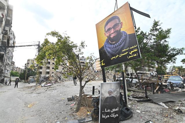 People check destruction behind posters of Hezbollah leader Naim Qassem (bottom) and a killed Hezbollah member in Beirut's southern suburbs after a 10-day ceasefire with Israel came into effect on April 17, 2026. A 10-day ceasefire deal struck between Lebanon and Israel took effect on April 17, sending displaced residents streaming south towards their homes, even as the Lebanese army warned of "a number of violations" in the area. (Photo by FADEL itani / AFP)