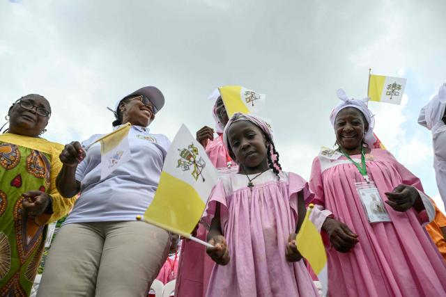 TOPSHOT - A young girl waves a Vatican flag while she gathers with other faithfuls as Pope Leo XIV leads the Holy Mass at the area in front of Japoma Stadium in Douala on the fifth day of an 11-day apostolic journey to Africa, on April 17, 2026. (Photo by Alberto PIZZOLI / AFP)