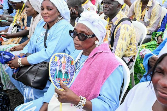 A faithful uses a fan, with the image of Pope Leo XIV on, to cool herself as the Pope leads the Holy Mass at the area in front of Japoma Stadium in Douala on the fifth day of an 11-day apostolic journey to Africa, on April 17, 2026. (Photo by Alberto PIZZOLI / AFP)