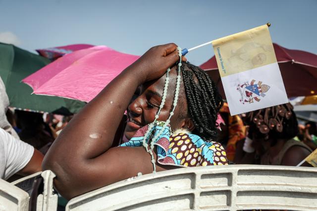 TOPSHOT - A faithful reacts while holding a rosary and a Vatican flag as Pope Leo XIV leads the Holy Mass at the area in front of Japoma Stadium in Douala on the fifth day of an 11-day apostolic journey to Africa, on April 17, 2026. (Photo by Daniel Beloumou Olomo / AFP)