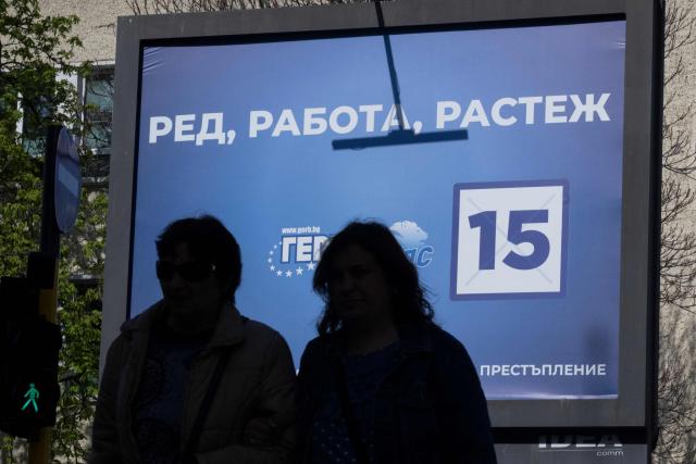 Pedestrians walk past an electoral billboard of the GERB party in Sofia on April 17, 2026. Bulgaria will hold its eighth general election in five years on April 19, 2026, with ex-president Rumen Radev's new grouping tipped to win a ballot many hope will end chronic instability. (Photo by Nikolay DOYCHINOV / AFP)