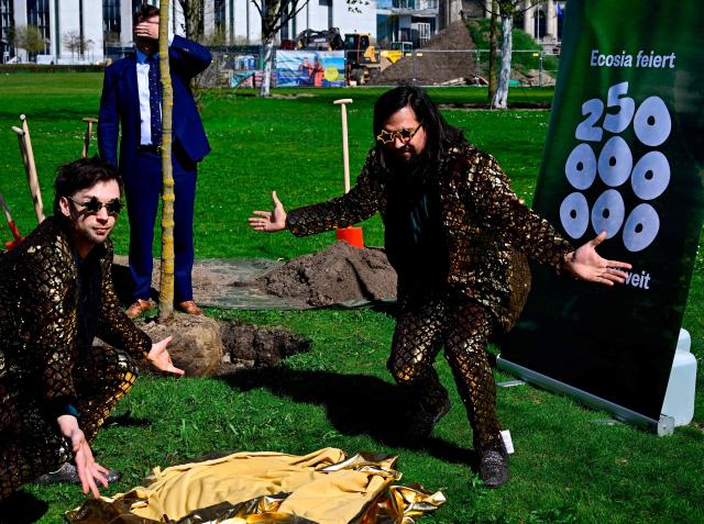 German Minister for the Environment, Climate Protection, Nature Conservation and Nuclear Safety Carsten Schneider (back C) hides behind a tree as he takes part in a ceremony to plant trees with magician duo Siegfried and Joy and online company Ecosia near the Reichstag building, seat of the German lower house of parliament, in Berlin on April 17, 2026. (Photo by Tobias SCHWARZ / AFP)