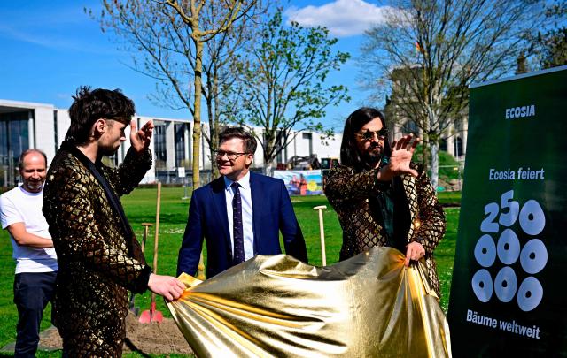 German Minister for the Environment, Climate Protection, Nature Conservation and Nuclear Safety Carsten Schneider (C) reacts as magician duo Siegfried and Joy perform during a ceremony to plant trees sponsored by online company Ecosia near the Reichstag building, seat of the German lower house of parliament, in Berlin on April 17, 2026. (Photo by Tobias SCHWARZ / AFP)