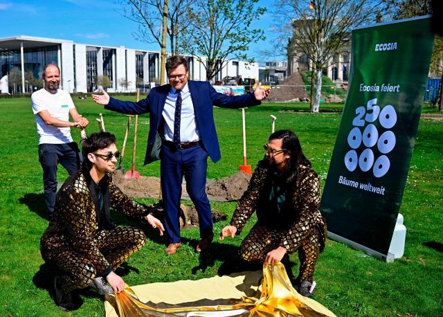 German Minister for the Environment, Climate Protection, Nature Conservation and Nuclear Safety Carsten Schneider (C) reacts as magician duo Siegfried and Joy perform during a ceremony to plant trees sponsored by online company Ecosia near the Reichstag building, seat of the German lower house of parliament, in Berlin on April 17, 2026. (Photo by Tobias SCHWARZ / AFP)