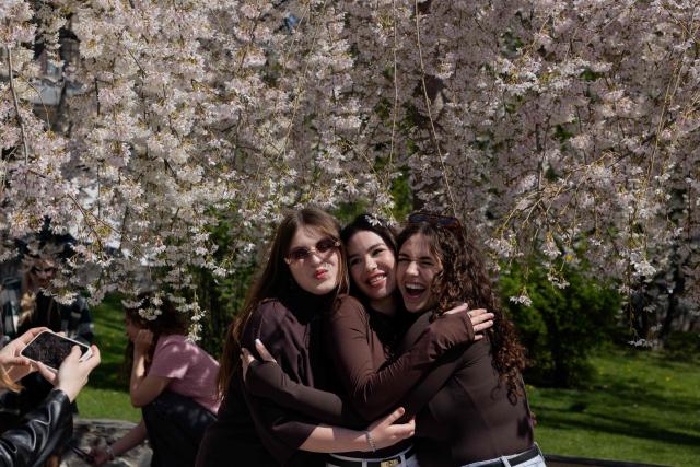 Local residents pose under a blooming tree in a park in Kyiv on April 17, 2026, amid the Russian invasion of Ukraine (Photo by Tetiana DZHAFAROVA / AFP)