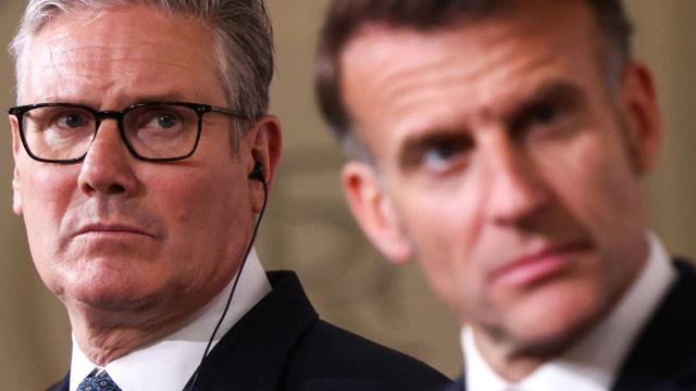 Britain's Prime Minister Keir Starmer (L) reacts behind France's President Emmanuel Macron as he attends a joint press conference following an international summit on efforts to reopen the Strait of Hormuz at the Elysee Presidential Palace in Paris on April 17, 2026. French President Emmanuel Macron and UK Prime Minister Keir Starmer chair a meeting of allies to consider sending a multinational force to ensure security and free-flowing trade in the Strait of Hormuz once the current conflict between Iran and the US and Israel ends. Iran imposed the blockade on the critical shipping bottleneck as soon as the US and Israel launched the war against the Islamic republic on February 28, leading to a surge in global energy prices. Even with a shaky ceasefire in place, the US is now imposing its own blockade on Iranian ports. (Photo by Tom Nicholson / POOL / AFP)