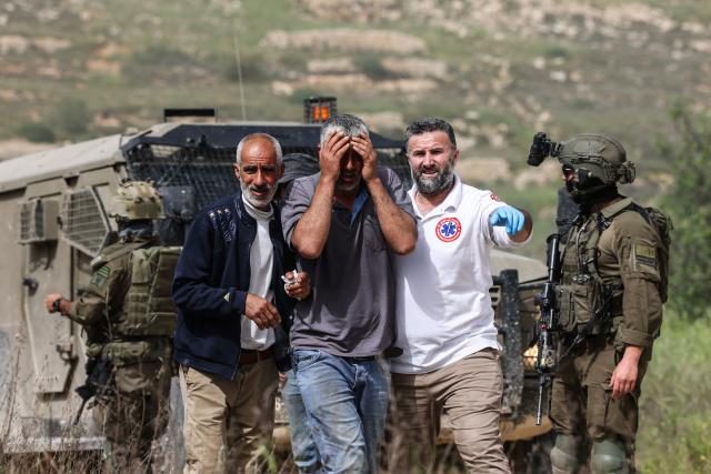 Israeli soldiers stand by as Palestinian medics assist a man who was reportedly attacked with pepper spray by Jewish settlers while he worked on his farmland near the Palestinian village of Halhoul, south of the Israel-occupied West Bank city of Hebron, on April 17, 2026. Violence in the Palestinian West Bank, which Israel has occupied since 1967, has soared since the Hamas attack on Israel triggered the Gaza war in October 2023. (Photo by HAZEM BADER / AFP)
