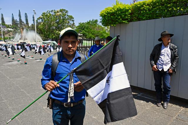 A demonstrator holds a black-and-white depiction of the Guatemalan flag outside the Palace of Justice during a protest against the nomination of Attorney General Consuelo Porras for a third term in Guatemala City on April 17, 2026. The official is seeking a third four-year term despite the United States, Canada, the United Kingdom and the European Union, along with around a dozen allied countries, revoking her visa for undermining democracy. (Photo by Johan ORDONEZ / AFP)