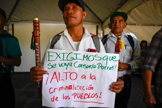 A man holds a sign reading “We demand Consuelo Porras’s resignation! Enough of criminalizing Indigenous peoples!” during a protest against the nomination of Consuelo Porras for a third term as attorney general outside the Palace of Justice in Guatemala City on April 17, 2026. The official is seeking a third four-year term despite the United States, Canada, the United Kingdom and the European Union, along with around a dozen allied countries, revoking her visa for undermining democracy. (Photo by Johan ORDONEZ / AFP)