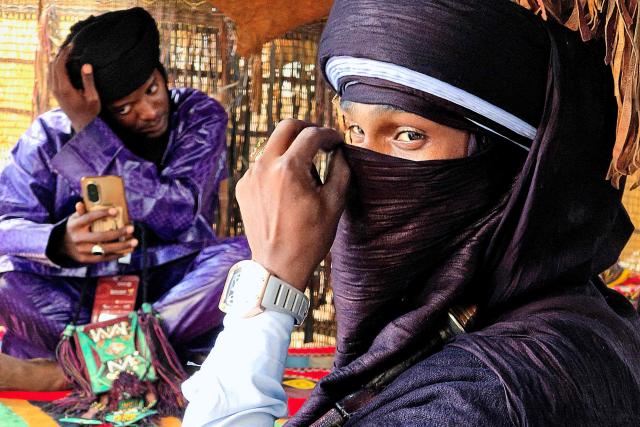 Two Libyan men adjust their traditional dress as they wait to entertain visitors during the 52nd Tripoli International Fair, which features some 285 local and foreign companies and is drawing large crowds in the Libyan capital Tripoli, on April 17, 2026. (Photo by Mahmud Turkia / AFP)
