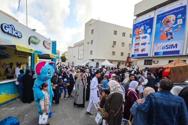 A child poses for a photograph with a cartoon caricature during the 52nd Tripoli International Fair, featuring some 285 local and foreign companies, is drawing large crowds of visitors in the Libyan capital of Tripoli on April 17, 2026. (Photo by Mahmud Turkia / AFP)
