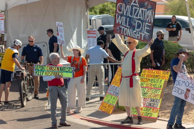 People hold signs as they protest the US president's visit to Arizona outside Dream City Church, where the Turning Point USA "Build the Red Wall" event is being held, in Phoenix, Arizona, on April 17, 2026. President Trump is in Arizona to speak at the Turning Point USA event, the conservative political organization founded by late activist Charlie Kirk. (Photo by Olivier Touron / AFP)