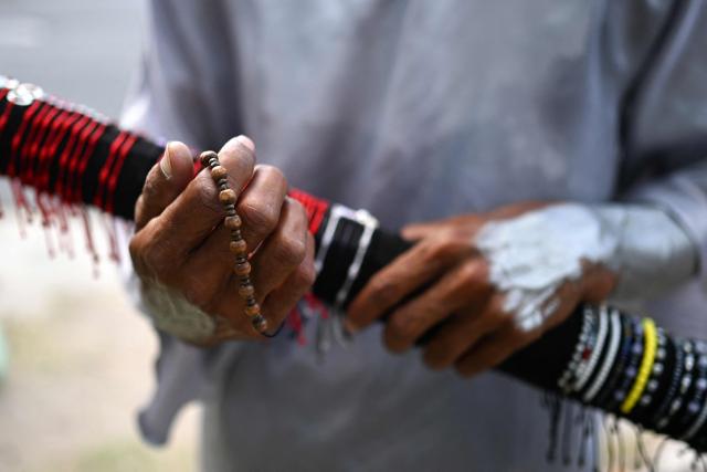 Street performer Samuel Gutierrez, 37, shows the bracelets he sells as he juggles sharp metal blades amid midday traffic in San Salvador on April 17, 2026. Samuel says that after ten years in the trade, he has performed on the main streets and avenues of San Salvador, earning between $5 and $10 a day, an income he supplements by selling bracelets and handicrafts he makes himself to cover his family’s expenses. (Photo by Marvin RECINOS / AFP)