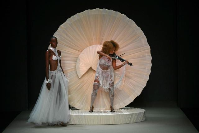 A model presents a creation by Helo Rocha while another plays the violin during Rio Fashion Week at Pier Maua in Rio de Janeiro, Brazil, on April 17, 2026. (Photo by Mauro PIMENTEL / AFP)