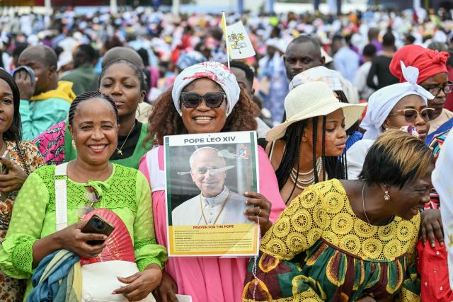 A faithful holds a poster of Pope Leo XIV as she gathers with others to wait for his arrival to lead the Holy Mass at the Yaounde Ville Airport in Yaounde on the sixth day of an 11-day apostolic journey to Africa, on April 18, 2026. (Photo by Alberto PIZZOLI / AFP)