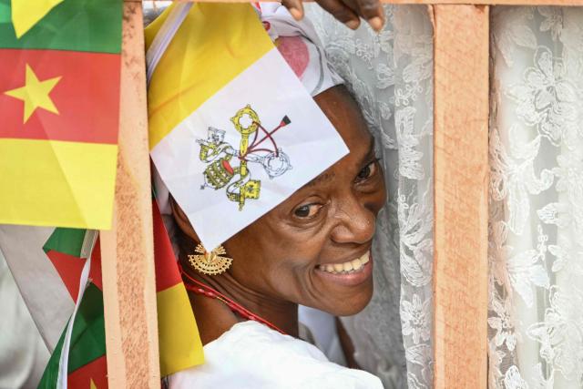 A faithful smiles as she gathers with others ahead of the arrival of Pope Leo XIV to lead a Holy Mass at the Yaounde Ville Airport in Yaounde on the sixth day of an 11-day apostolic journey to Africa, on April 18, 2026. (Photo by Alberto PIZZOLI / AFP)