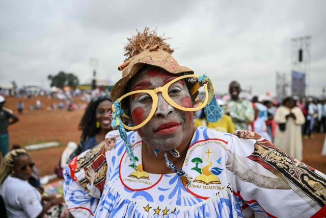 TOPSHOT - A faithful wearing over-sized glasses poses for a photograph as she gathers with others ahead of the arrival of Pope Leo XIV to lead a Holy Mass at the Yaounde Ville Airport in Yaounde on the sixth day of an 11-day apostolic journey to Africa, on April 18, 2026. (Photo by Alberto PIZZOLI / AFP)