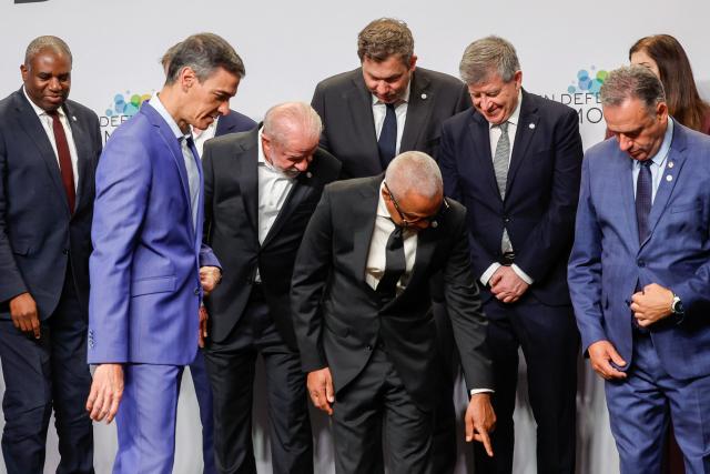 Cape Verde's President Jose Maria Neves (C) points to a name tag as leaders including Britain's Deputy Prime Minister and Justice Secretary David Lammy (L), Spain's Prime Minister Pedro Sanchez (2L) and  Brazilian President Luiz Inacio Lula Da Silva (3L) look for their positions before a family photo at a "Meeting in Defence of Democracy", a meeting of leftist leaders seeking to rally against the threat to democracy from the far right in Barcelona on April 18, 2026. The gathering comes as democratic institutions and values have faced growing threats around the globe from advancing authoritarian and far-right forces in the age of US President Donald Trump. Many of the participants will take part in the first edition of the so-called "Global Progressive Mobilisation" which will be held in the same venue. (Photo by Oscar DEL POZO / AFP)