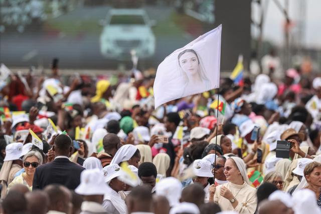 A faithful holds a flag as she gathers with others as Pope Leo XIV arrives to lead a Holy Mass at the Yaounde Ville Airport in Yaounde on the sixth day of an 11-day apostolic journey to Africa, on April 18, 2026. (Photo by Daniel Beloumou Olomo / AFP)