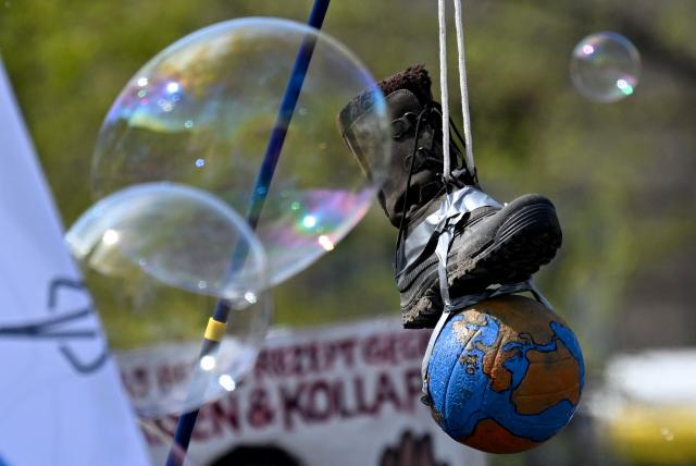 Soap bubbles float past an installation of a boot stepping on the earth during a demonstration of activists and supporters of Fridays for Future, Campact and others against the German government's energy policy, on April 18, 2026 in Berlin. Activists call for faster expansion of solar and wind energy, rapid development of distribution grids, storage and digitalization, a strong European clean energy industry, lower electricity taxes and cheaper power for heat pumps, as well as social support and tenant protection to ensure affordable, climate-friendly heating. (Photo by RALF HIRSCHBERGER / AFP)