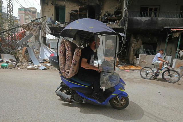 A displaced resident along with his belongings ride a scooter past a burnt building as he returns back to a neighborhood in Beiruts southern suburbs, on April 18, 2026. Lebanese President Joseph Aoun said on April 17 that his country was on the verge of a "new phase" of "permanent agreements", after the 10-day ceasefire in the Israel-Hezbollah war went into force. Lebanon was drawn into the Middle East conflict on March 2 when Tehran-backed Hezbollah attacked Israel to avenge the death of Iranian supreme leader Ali Khamenei. (Photo by Ibrahim AMRO / AFP) / 