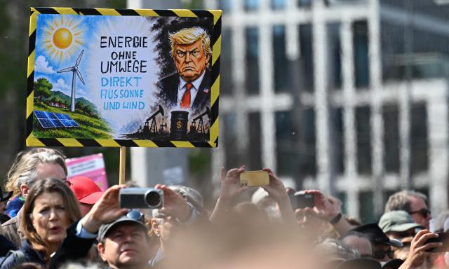Protesters hold up a placard depicting US President Donald Trump with fossile energies and on the other side alternative energies, reading "Energy without detour - directly from sun and wind", during a demonstration of activists and supporters of Fridays for Future, Campact and others against the German government's energy policy, on April 18, 2026 in Berlin. Activists call for faster expansion of solar and wind energy, rapid development of distribution grids, storage and digitalization, a strong European clean energy industry, lower electricity taxes and cheaper power for heat pumps, as well as social support and tenant protection to ensure affordable, climate-friendly heating. (Photo by RALF HIRSCHBERGER / AFP)