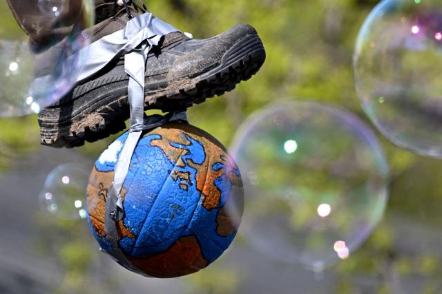 Soap bubbles float past an installation of a boot stepping on the earth during a demonstration of activists and supporters of Fridays for Future, Campact and others against the German government's energy policy, on April 18, 2026 in Berlin. Activists call for faster expansion of solar and wind energy, rapid development of distribution grids, storage and digitalization, a strong European clean energy industry, lower electricity taxes and cheaper power for heat pumps, as well as social support and tenant protection to ensure affordable, climate-friendly heating. (Photo by RALF HIRSCHBERGER / AFP)