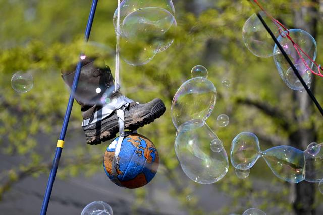 Soap bubbles float past an installation of a boot stepping on the earth during a demonstration of activists and supporters of Fridays for Future, Campact and others against the German government's energy policy, on April 18, 2026 in Berlin. Activists call for faster expansion of solar and wind energy, rapid development of distribution grids, storage and digitalization, a strong European clean energy industry, lower electricity taxes and cheaper power for heat pumps, as well as social support and tenant protection to ensure affordable, climate-friendly heating. (Photo by RALF HIRSCHBERGER / AFP)