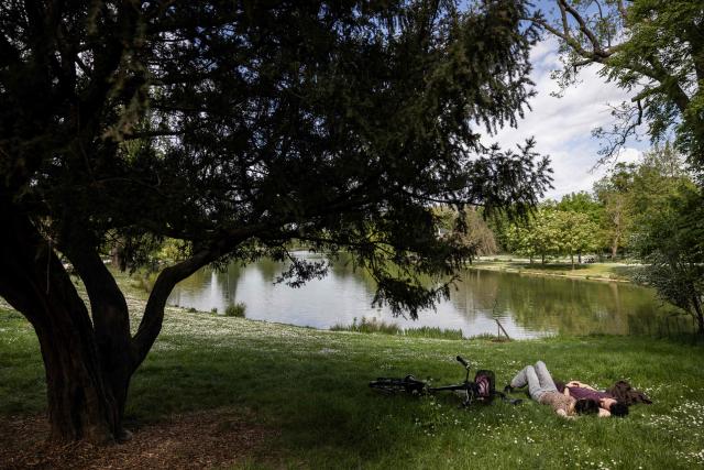 A couple lie on the grass by the Daumesnil Lake at the Bois de Vincennes park in Paris on April 18, 2026. (Photo by Behrouz MEHRI / AFP)