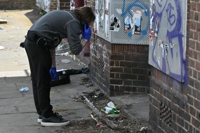 A police officer looks at a glass bottle during an investigation into an arson attack, beside the business "Jewish futures" in Hendon, north London on April 18, 2026. Counter-terrorism police are investigating an arson attack that targeted a business in an area with a large Jewish community in northwest London, the British capital's police said April 18, 2026, following several similar incidents in recent weeks. (Photo by JUSTIN TALLIS / AFP)